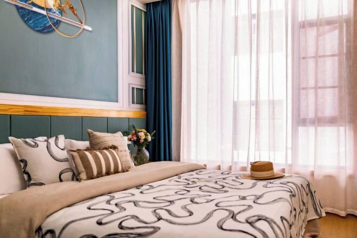 A bedroom with a bed, pillows, a hat, and a wall decoration.