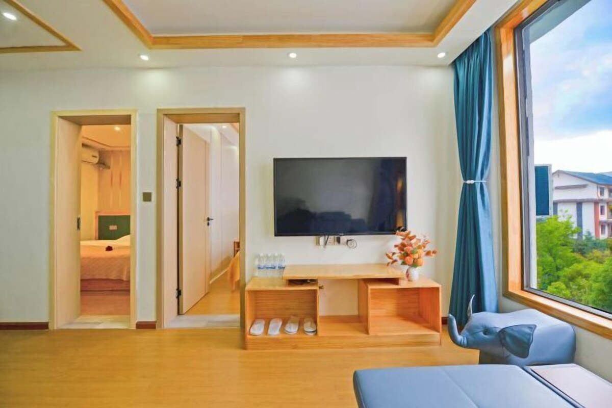 A hotel room with a TV, a desk with a chair, a bed, and a window with curtains.
