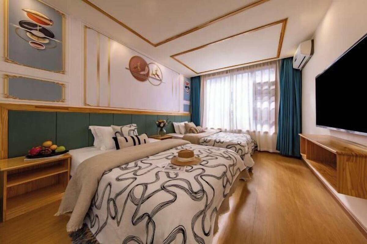 A hotel room with two beds, a large TV, and a wooden floor.