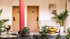 Un vestíbulo de hotel con dos puertas de madera, un sofá blanco, una mesa de centro con frutas y plantas en macetas.