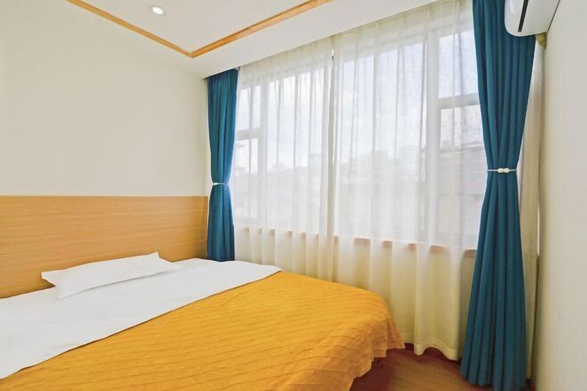 A hotel room with a bed, a window with curtains, and an air conditioning unit.