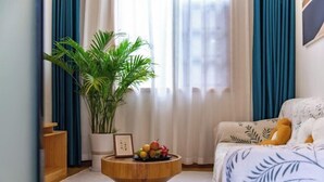 Un dormitorio acogedor con cama, una mesa redonda de madera con fruta y un cuadro enmarcado, una planta en maceta y un cojín blanco mullido.