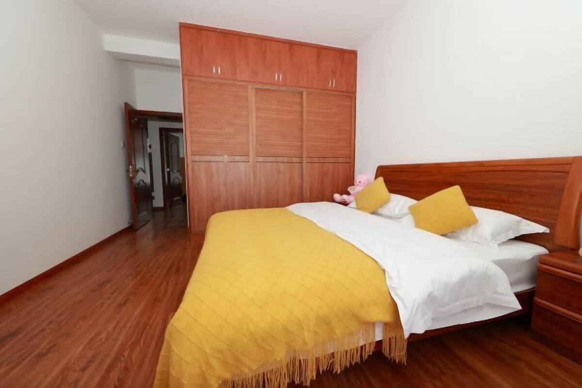 A bedroom with a wooden wardrobe, a bed with yellow and white bedding, and a wooden headboard.