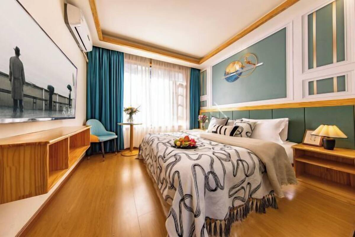 A hotel room with a bed, a desk, a chair, a TV, and a window with curtains.