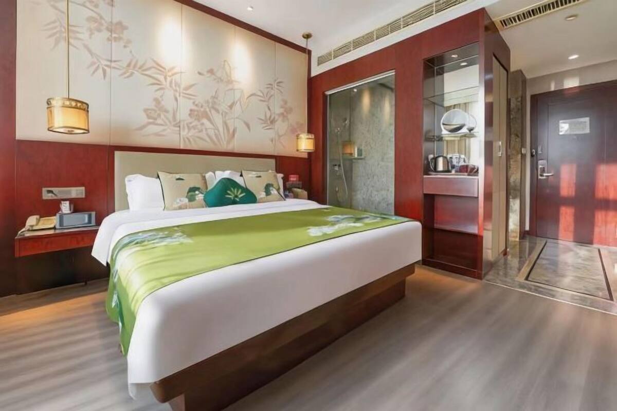 Une chambre d’hôtel avec un grand lit, une table de chevet avec une lampe, une armoire et un espace douche.