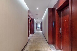Ein langer, schmales Hotel-Flur mit Türen an beiden Seiten, Teppichboden und Einbauleuchten.