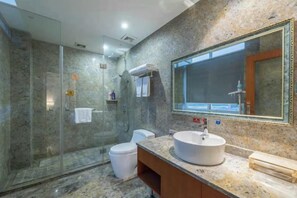 Une salle de bain moderne avec une douche à parois de verre, des toilettes blanches, un comptoir en marbre et un grand miroir.