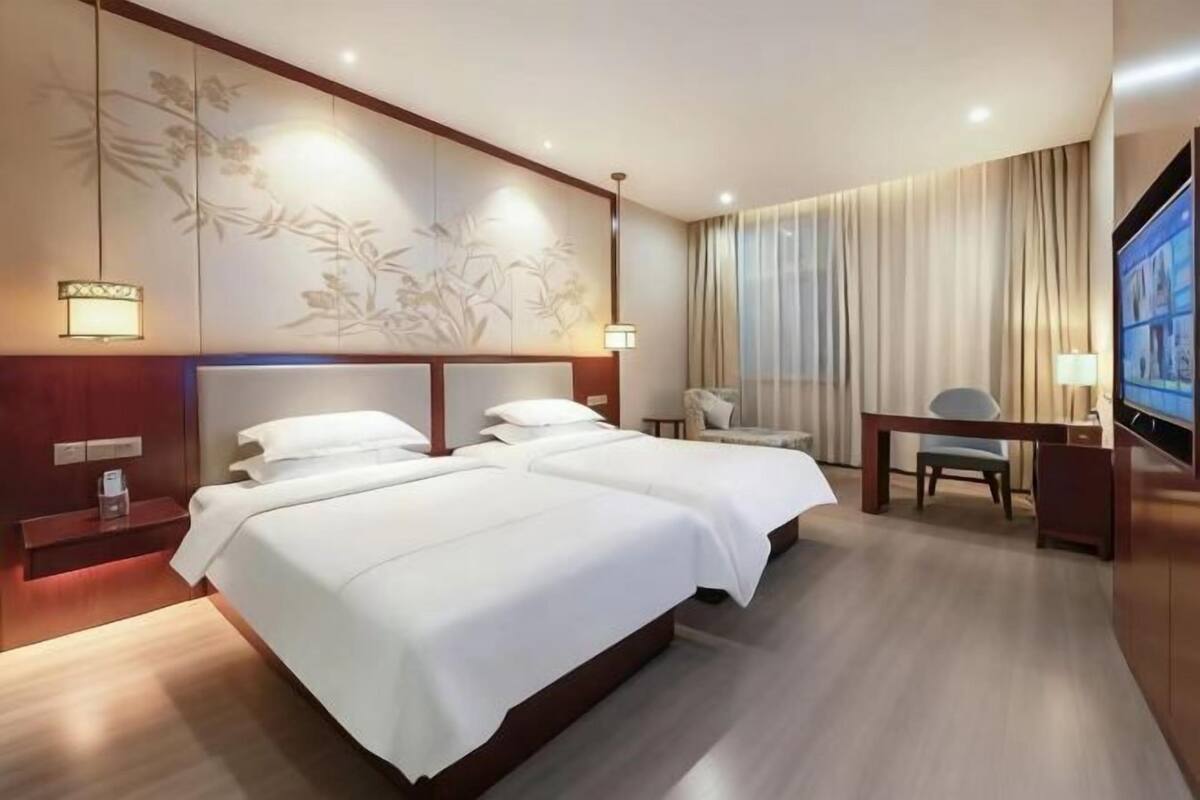 Une chambre d’hôtel avec deux lits, un bureau, une chaise, une télévision et un panneau décoratif mural.