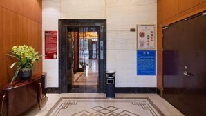 Eine Hotelhalle mit Marmorboden, Holzvertäfelung, einer Topfpflanze, einem Mülleimer und Hinweisschildern.