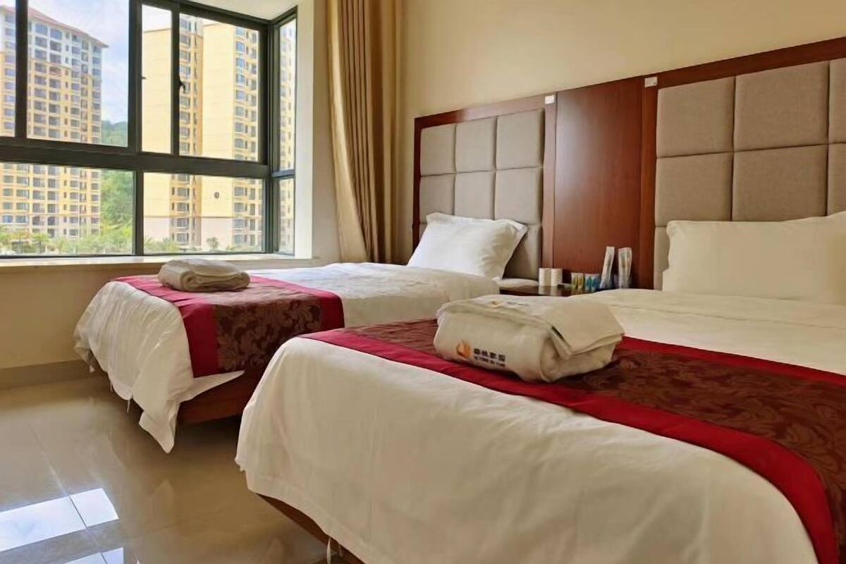 A hotel room with two beds, a large window, and a view of high-rise buildings.
