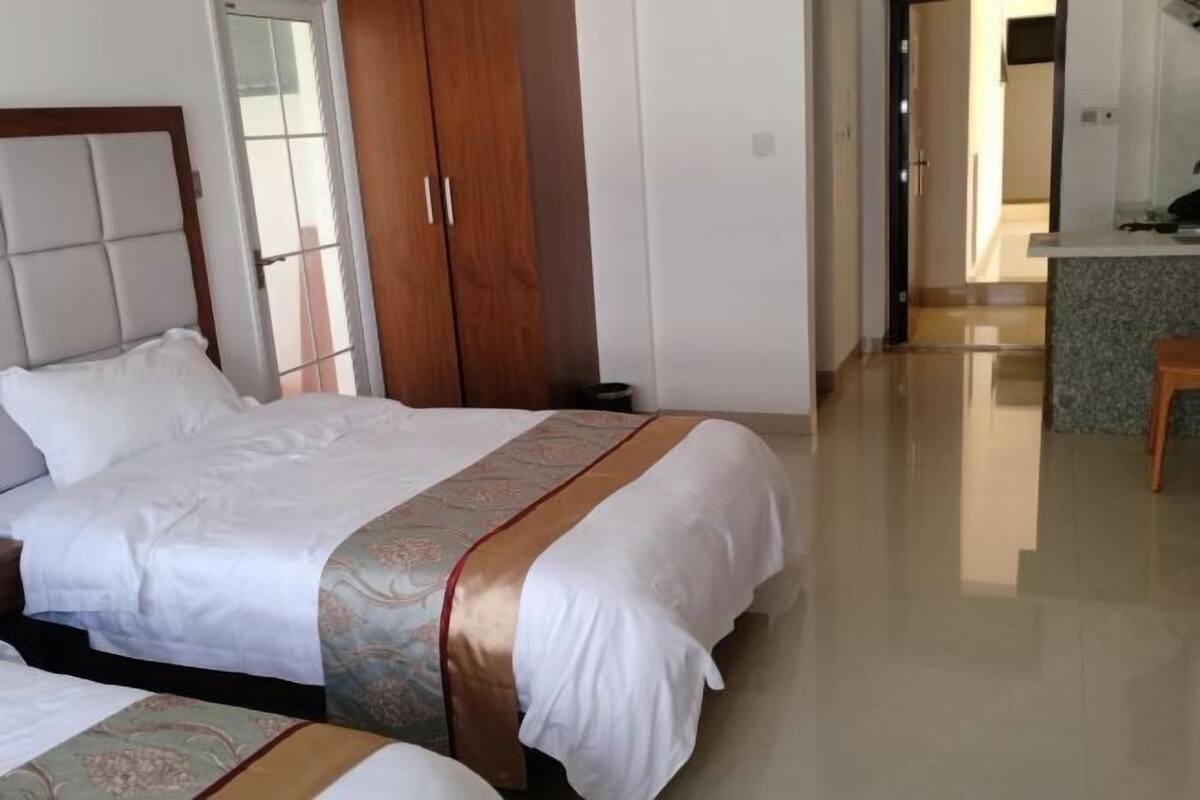A hotel room with two beds, a wardrobe, a bathroom, and a kitchenette.