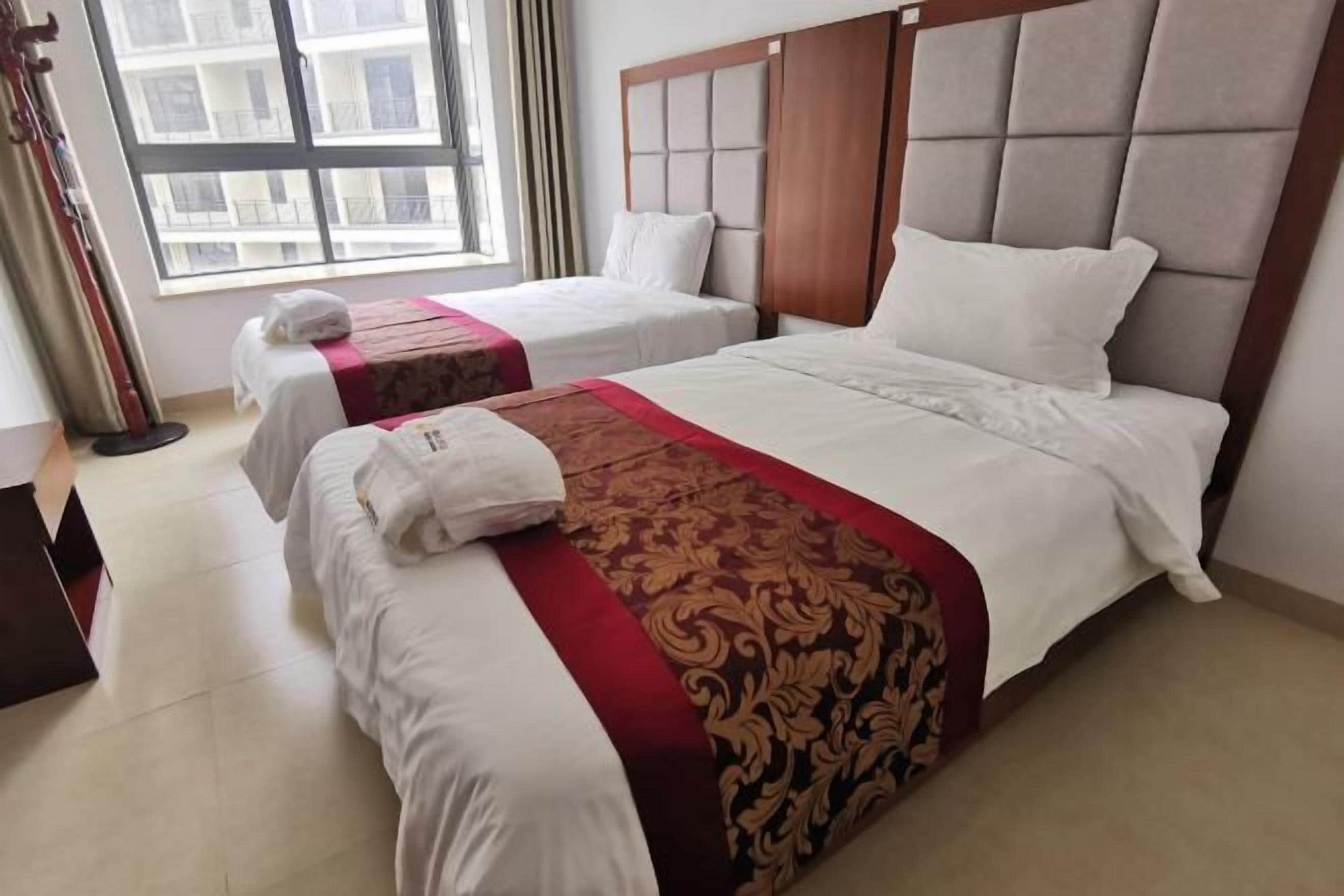 A hotel room with two beds, a large window, and a view of buildings outside.