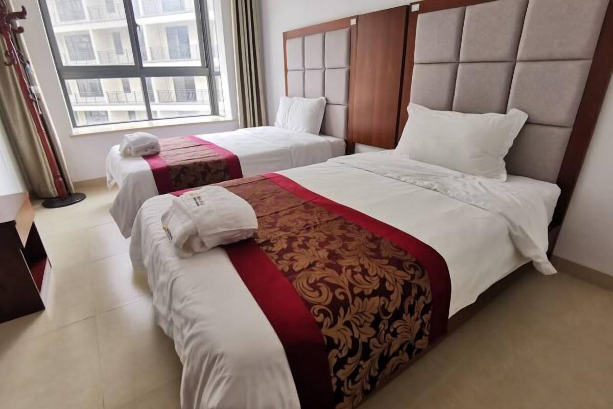 A hotel room with two beds, a large window, and a view of the cityscape.