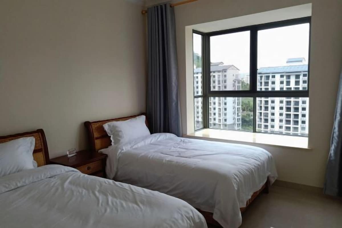 A hotel room with two beds, a large window, and a view of buildings outside.