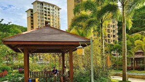 A gazebo in a lush garden with a view of high-rise buildings in the background. - Coconut Maple Home Apartment (Wuzhishan)
