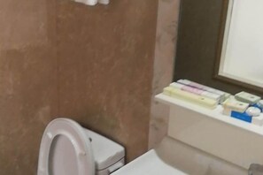 A bathroom with a toilet, a mirror, and a shelf with toiletries. - Shunda Business Inn (Guangde)