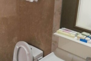 A bathroom with a toilet, a mirror, and a shelf with toiletries.