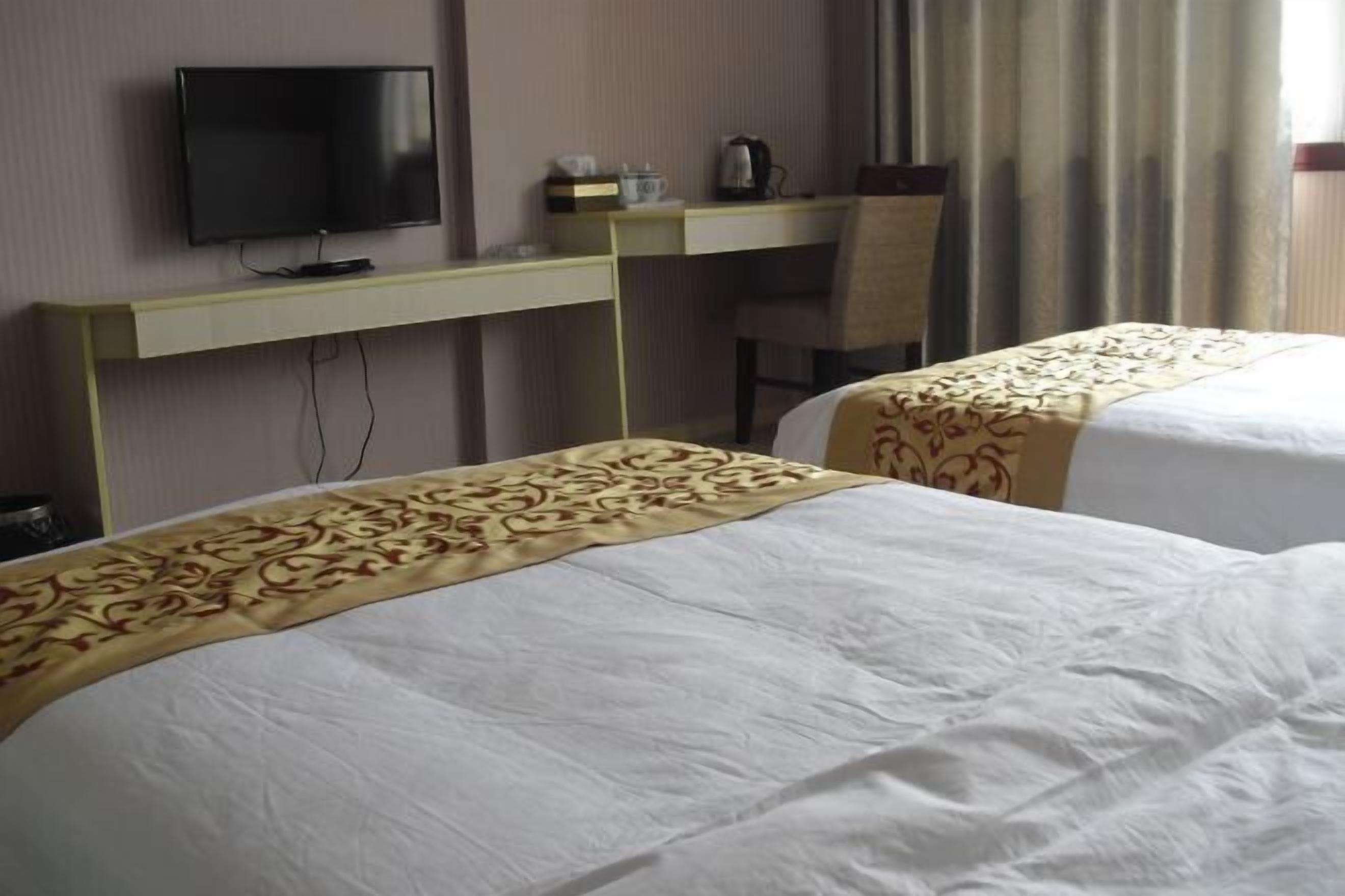 Quarto de hotel com duas camas, uma televisão, uma escrivaninha e uma cadeira.