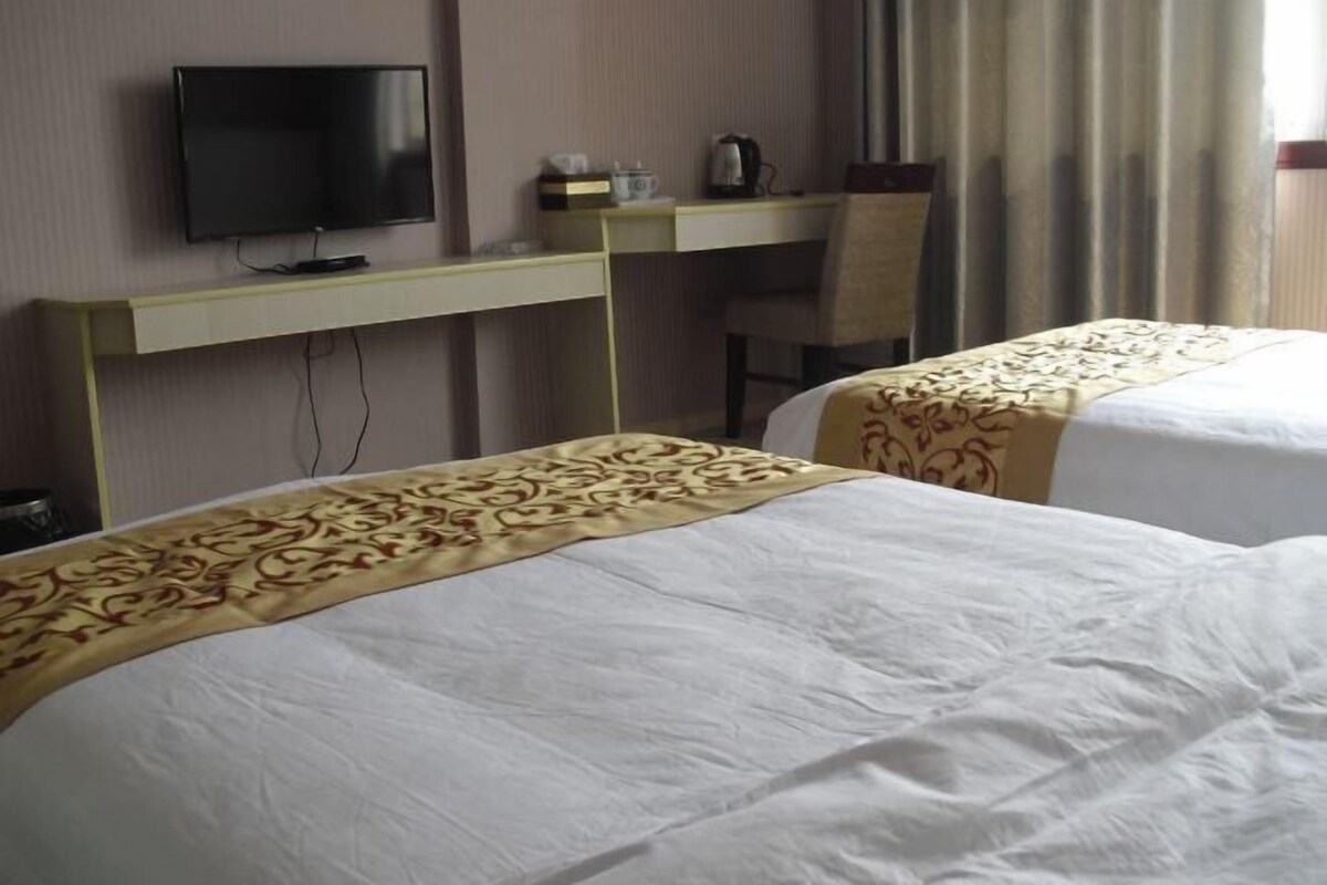 A hotel room with two beds, a TV, a desk, and a chair.