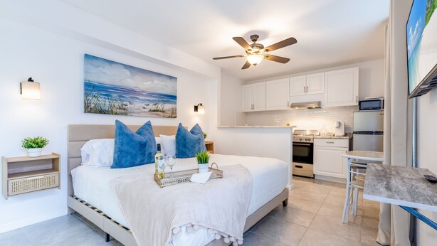 A modern bedroom with a large bed, a ceiling fan, and a painting of a beach scene. - Date me ,Top Location , Close Beach  (Greenacres)