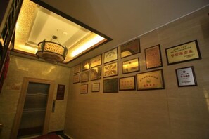 A hallway with framed awards on the wall, an elevator, and a ceiling light fixture. - Chaxiang Hotel (Ning'er)