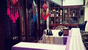 A room with a purple-striped tablecloth, a wicker chair, and a bookshelf with various items. - Chaxiang Hotel (Ning'er)