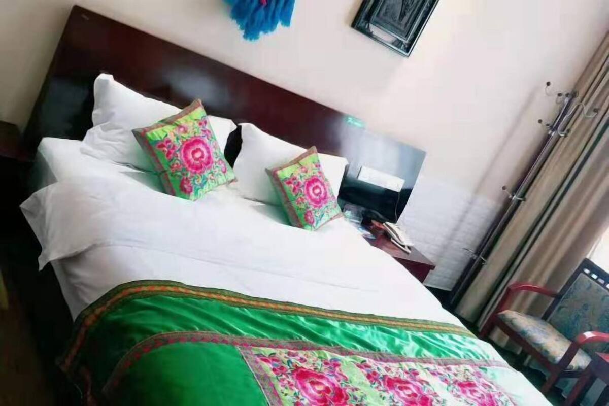 A neatly made bed with white linens and floral-patterned pillows, a wooden headboard, and a small bedside table with a lamp.
