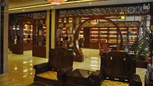 A lobby with traditional wooden furniture, a central decorative arch, and a well-lit area with shelves displaying various items. - Chaxiang Hotel (Ning'er)