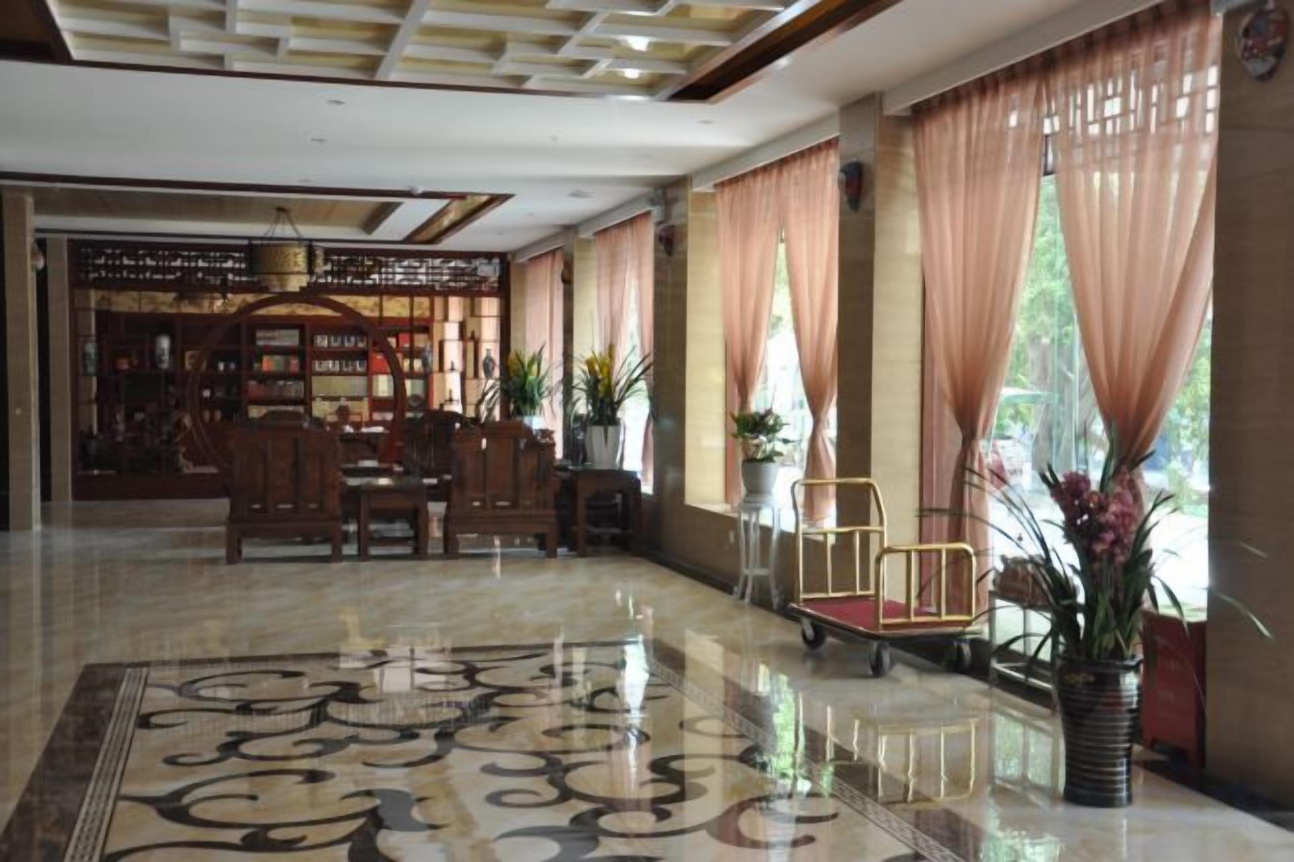 A hotel lobby with a polished floor, seating area, and large windows with curtains.