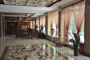 Un hall d’hôtel doté d’un sol ciré, d’un espace salon et de grandes fenêtres avec des rideaux.