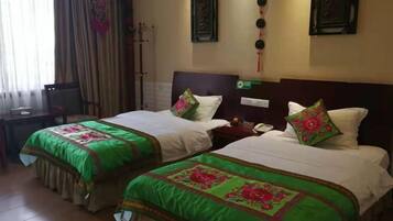 Une chambre d’hôtel avec deux lits, chacun recouvert d’une couvre-lit à motifs floraux verts et rouges, agrémentée de deux oreillers blancs et d’une table de chevet avec une lampe.