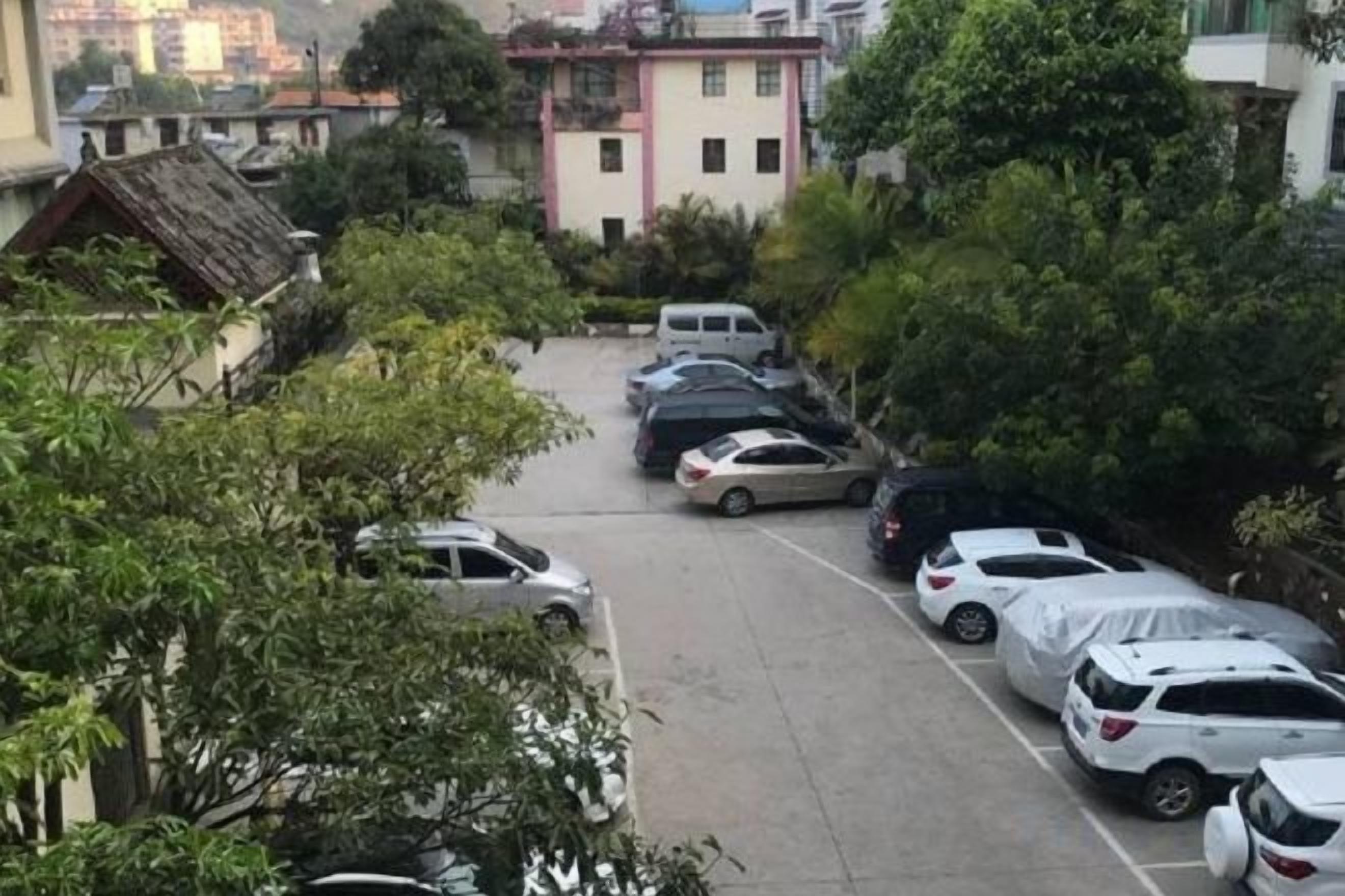 A parking lot with multiple cars parked in rows, surrounded by trees and buildings.
