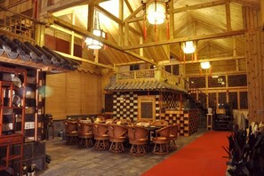 Un intérieur traditionnel en bois, avec un espace central dédié à la salle à manger, un escalier et un motif de carreaux au sol.