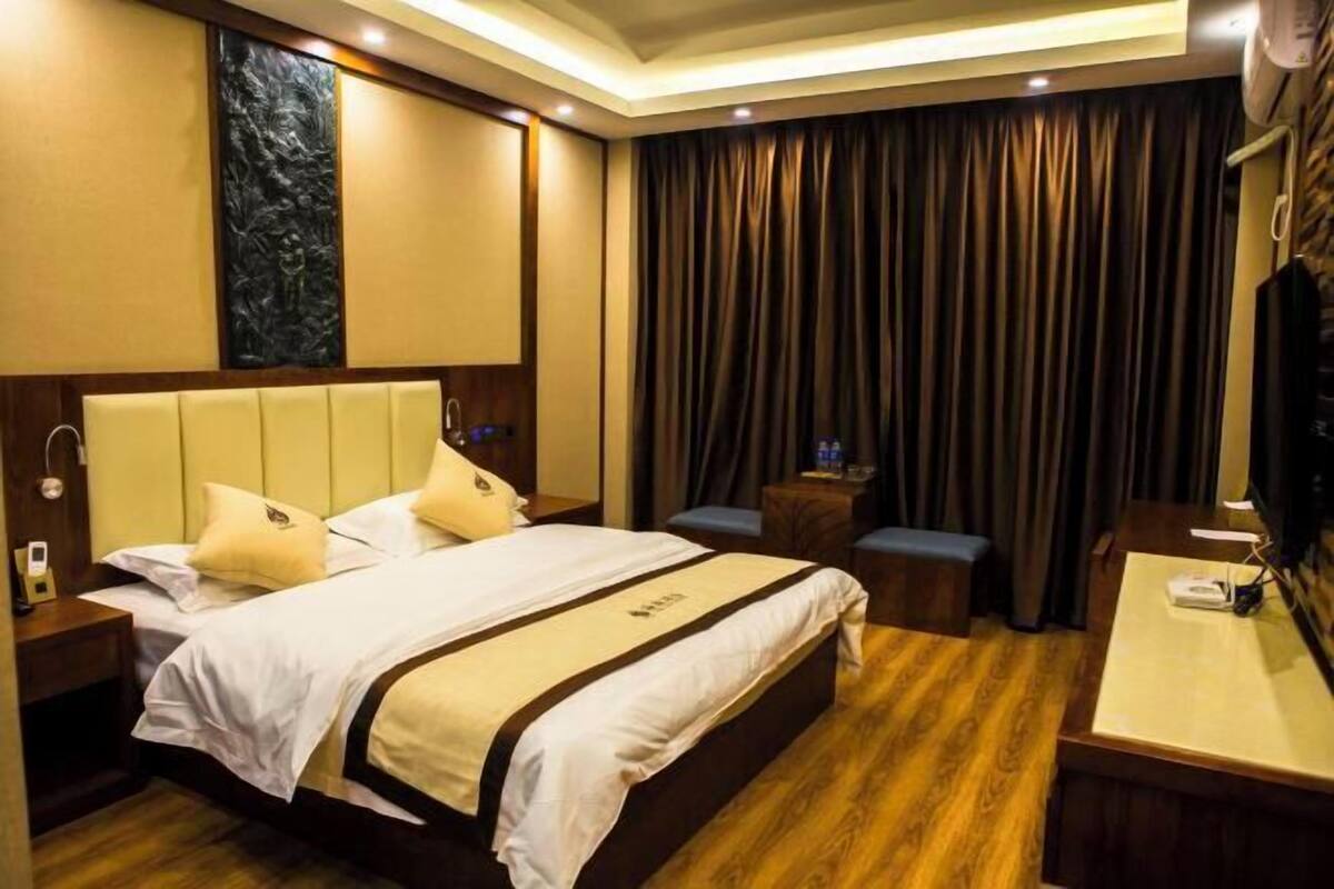 Ein Hotelzimmer mit einem großen Bett, einem Schreibtisch, einem Stuhl, einem kleinen Tisch, einem Fernseher und einem Vorhang.