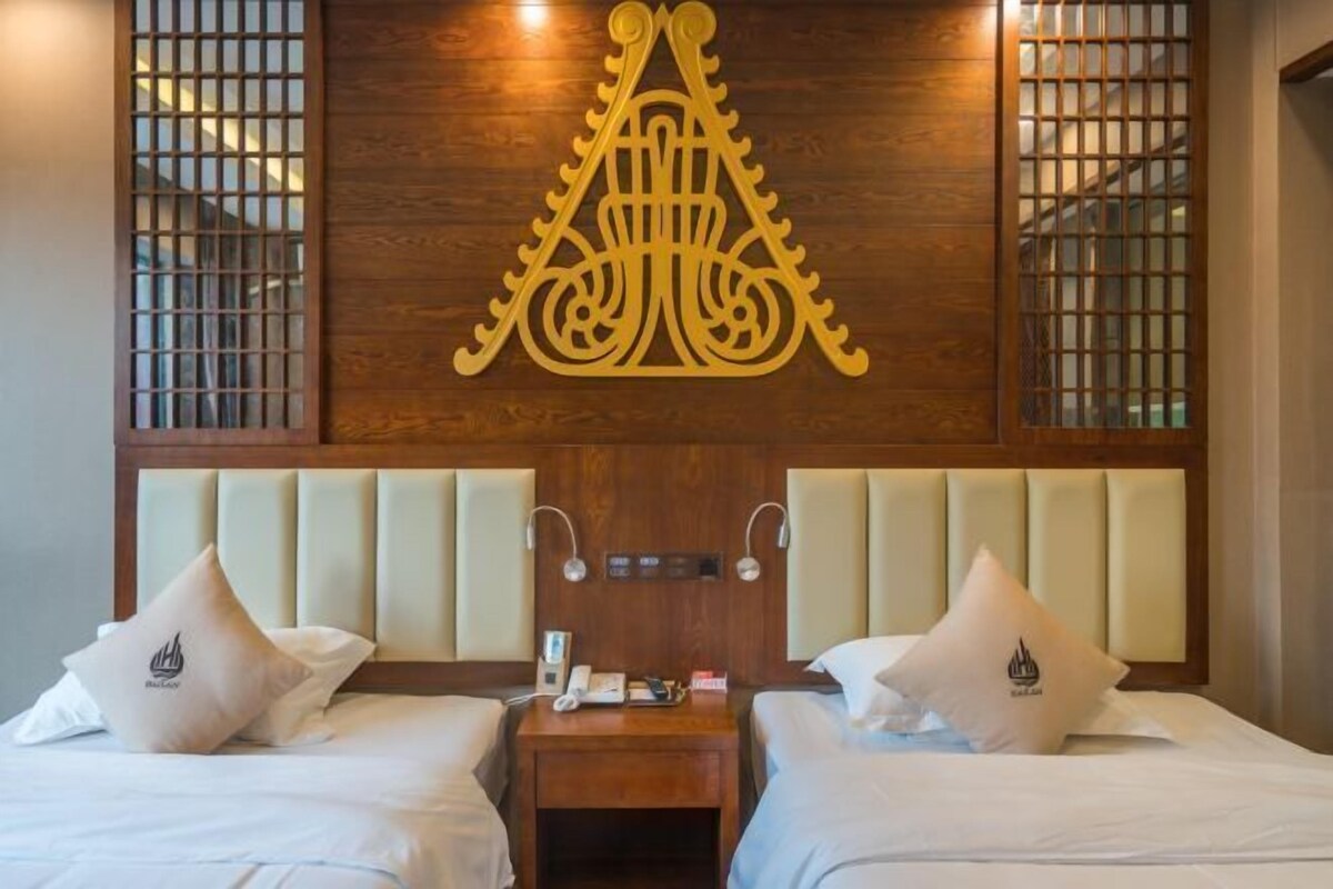 A hotel room with two beds, a wooden headboard, a decorative wall piece, and a nightstand with a phone and lamp.