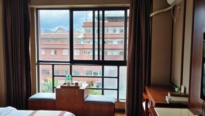 A hotel room with a large window, a bed, a wooden bench, and a desk. - Hai Lan Hotel (Lancang)