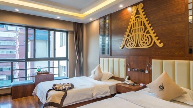 A hotel room with two beds, a large window, and a decorative wall piece. - Hai Lan Hotel (Lancang)