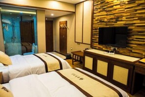 A hotel room with two beds, a TV mounted on a wooden wall, a small table, and a mirror.