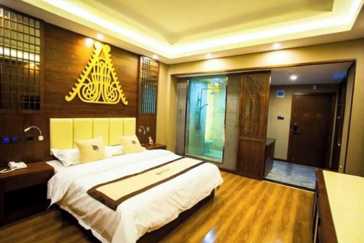 Ein Hotelzimmer mit einem großen Bett, Holzboden, einer Wanddekoration, einer Schiebetür zum Badezimmer und einem kleinen Schreibtisch mit Lampe.