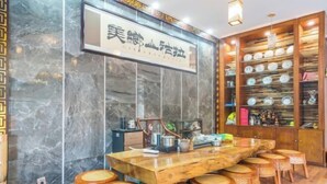 A dining area with a marble wall, a wooden table, and wicker stools. - Hai Lan Hotel (Lancang)