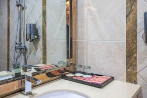 A modern bathroom with a large mirror, a shower, and a vanity with a tray of toiletries.