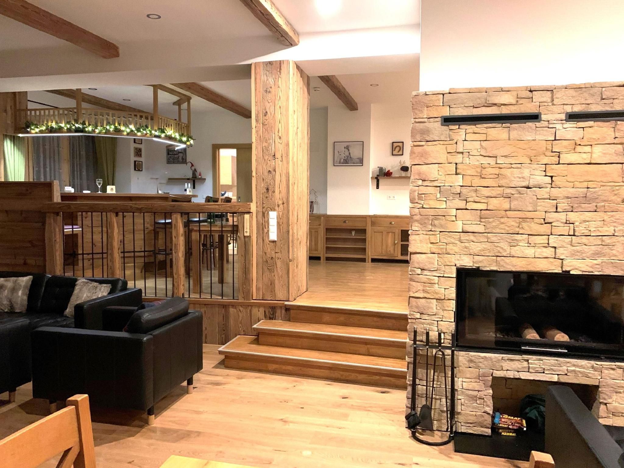 A modern living room with a stone fireplace, wooden flooring, and a black leather sofa.