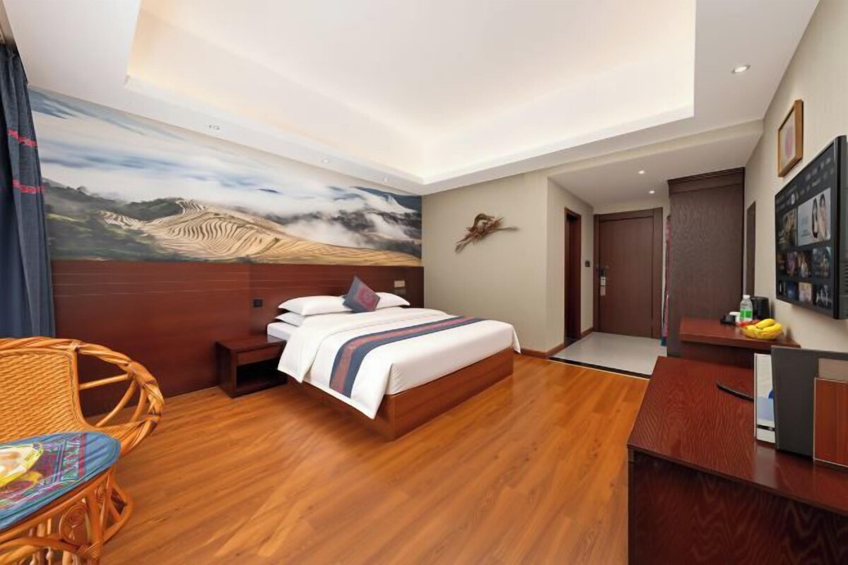 Habitación de hotel con cama, escritorio, silla y un mural en la pared.