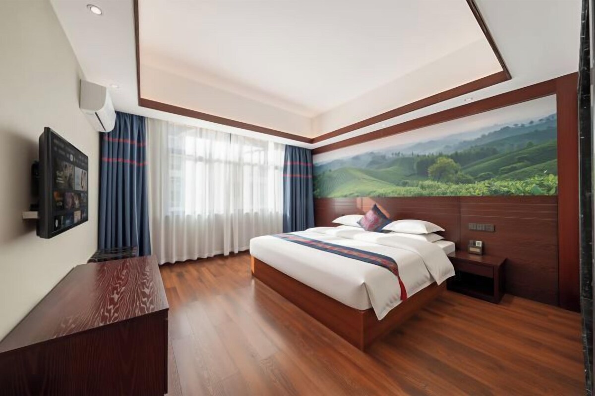 Habitación de hotel con una cama grande, un escritorio de madera, un televisor de pantalla plana y una vista panorámica del paisaje a través de una ventana.