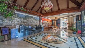 A lobby with a reception desk, a stone wall, a chandelier, and a circular emblem on the floor. - Mijng Qiyuan Minority Theme Hotel (Mojiang)