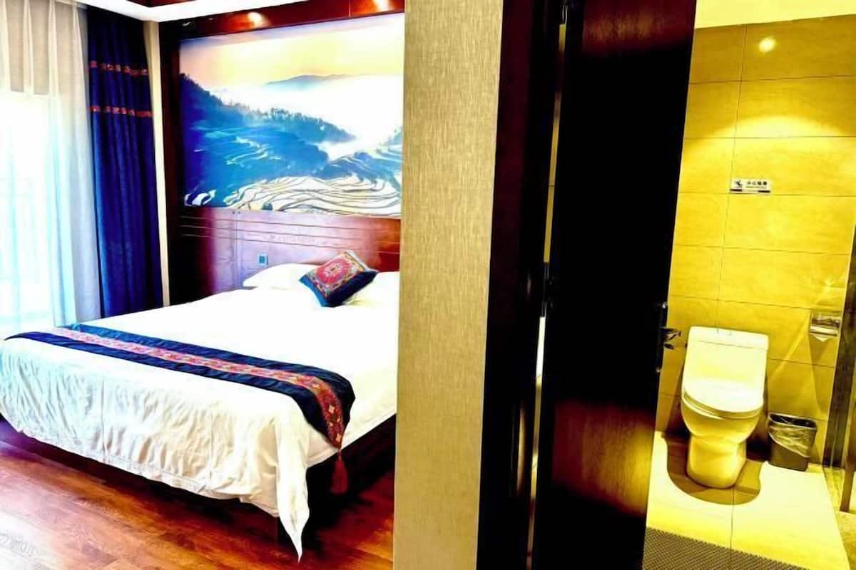 A hotel room with a bed, a painting on the wall, and a bathroom with a toilet.