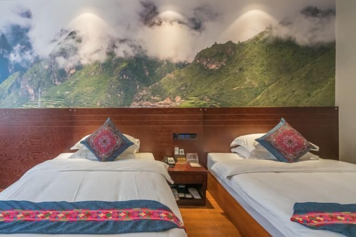 A hotel room with two beds, a nightstand, and a wall mural of a mountain landscape.