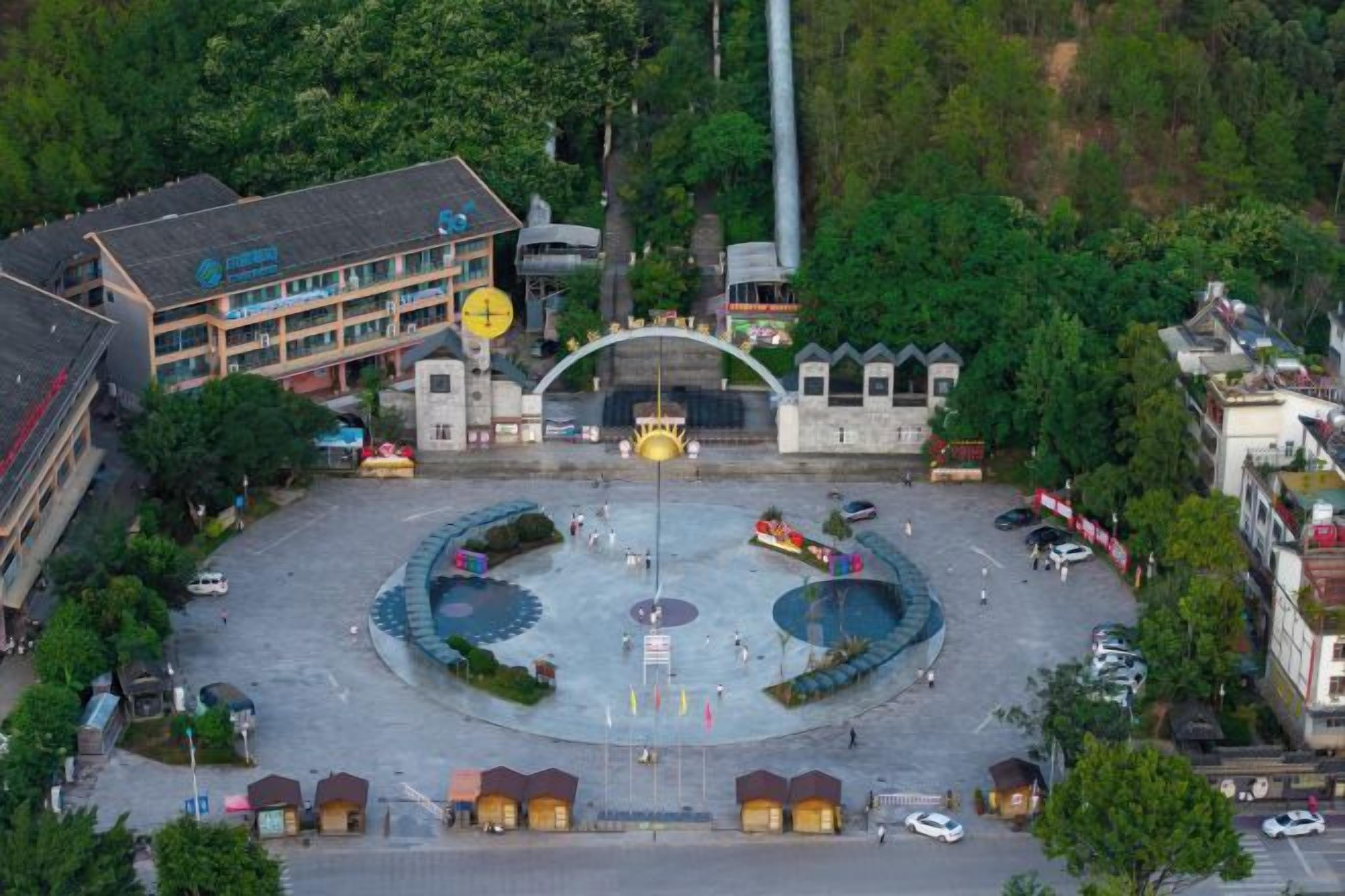 An aerial view of a square with a central fountain, surrounded by buildings and trees.