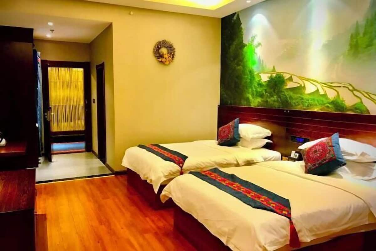 A hotel room with two beds, a wooden floor, a wall mural, and a door leading to another room.