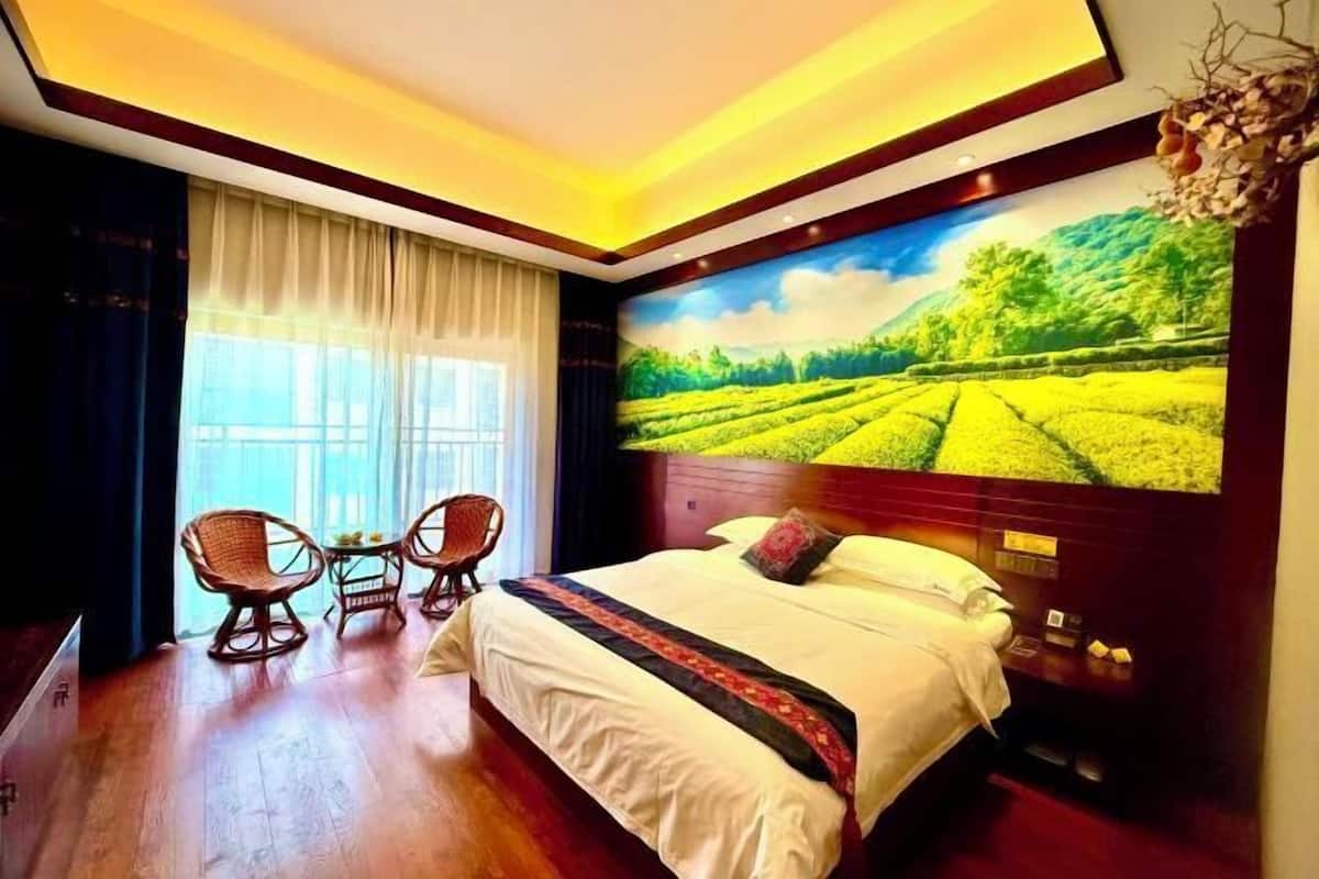 A hotel room with a large bed, a wall-mounted TV, a window with curtains, and a small table with chairs.